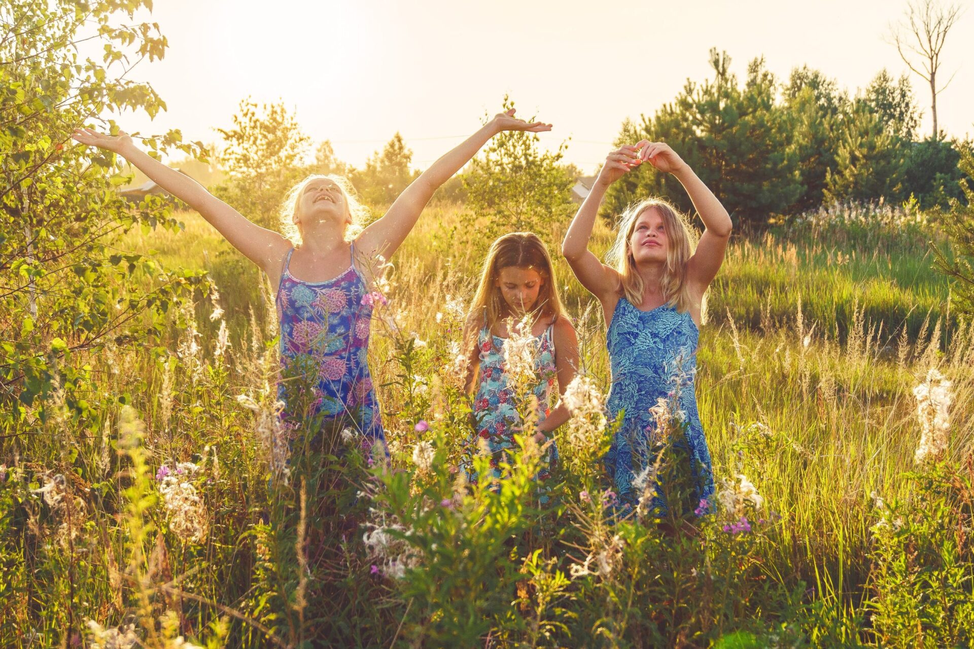 Girls in field raising arms up to the sky with flowers
